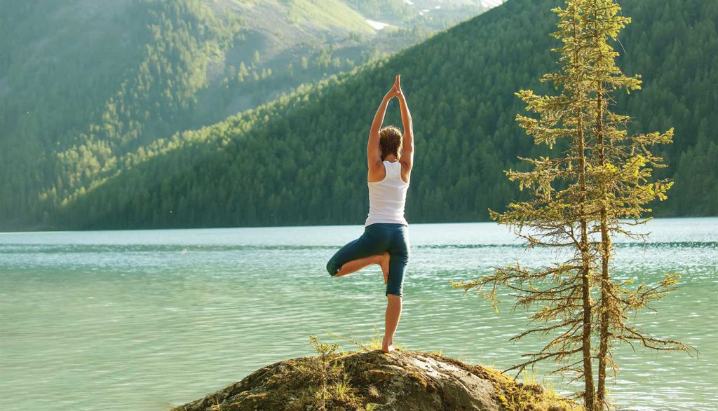 Mujer practicando yoga junto al río Ganges en Rishikesh 